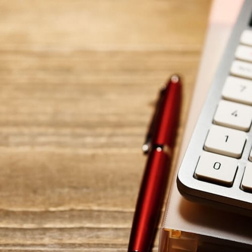 Zoom up view with white and gray keyboard on binder next to red pen on wooden table