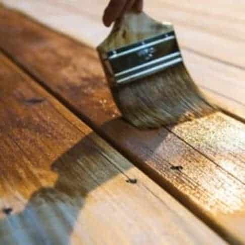 Paint brush with brown wooden handle and bristles painting dark brown wood stain on wooden panels