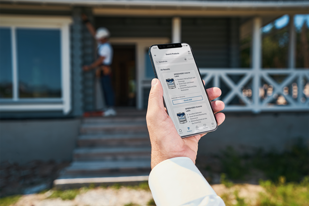 Person holding phone looking at PPG paint buckets with blurred front porch and person in background
