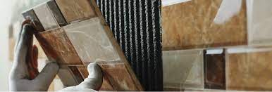 Person with gloves installing multi-brown hue stacked tiles onto wall