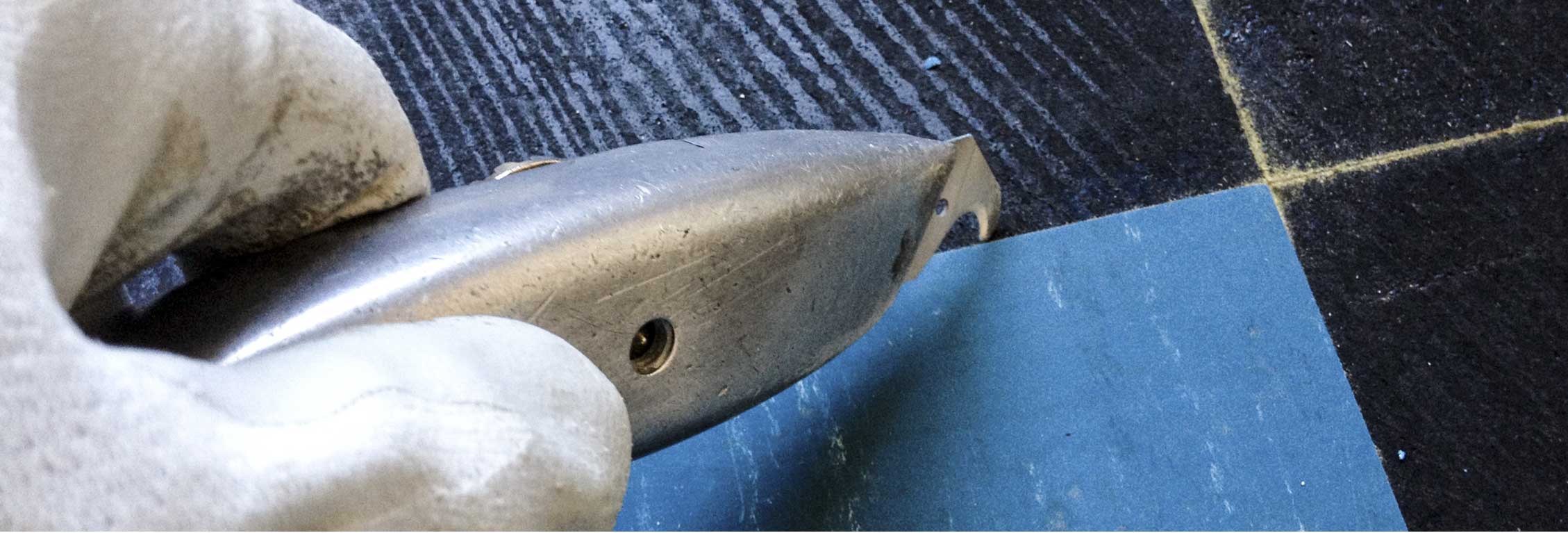 Person wearing glove using metal tool on wood