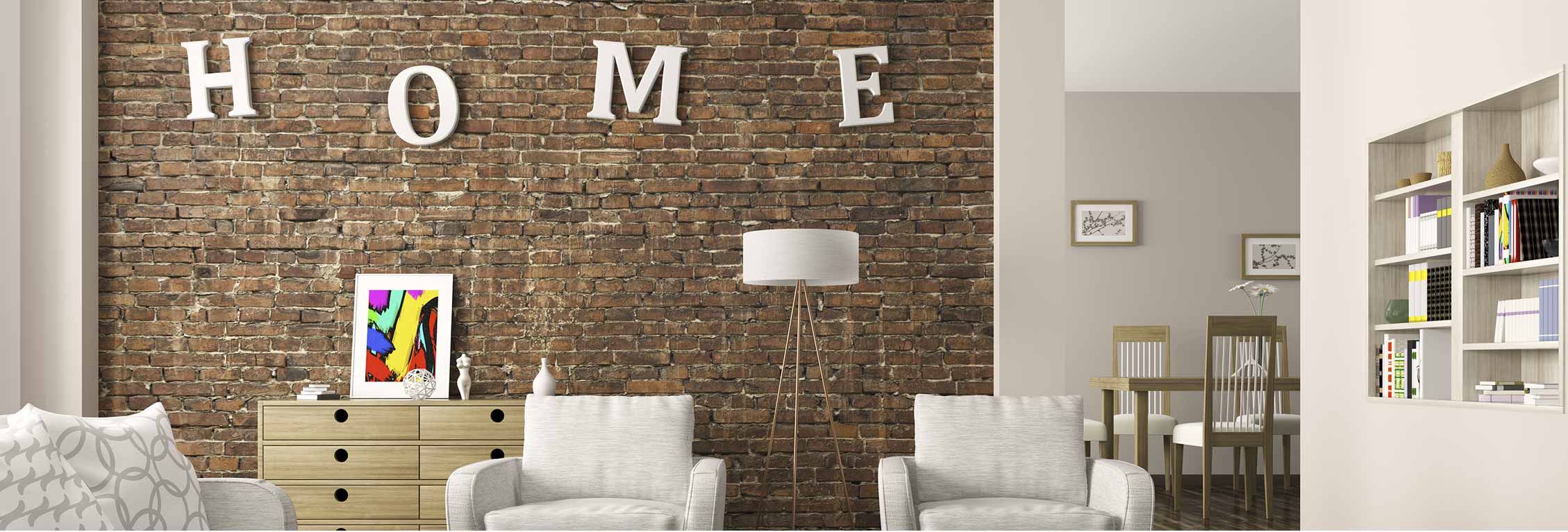 Gray wall room with gray furniture, brown brick wall in foreground with decorative word "HOME" on wall with colorful painting leaning on drawers