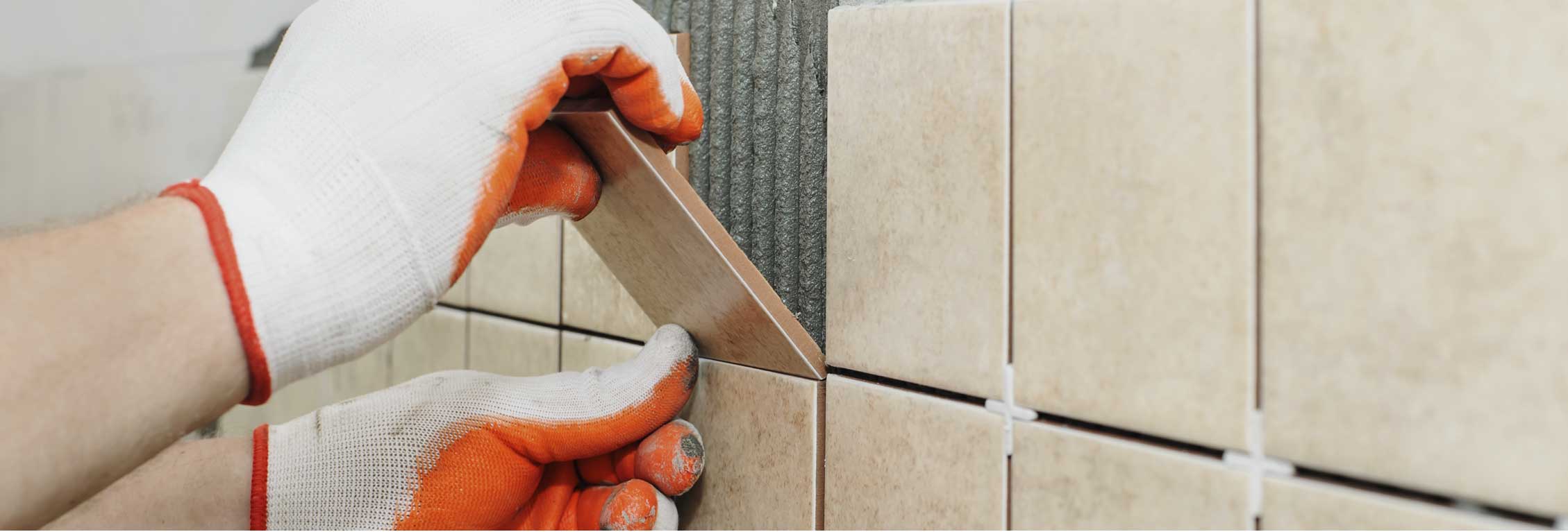 Person with gloves applying tan ceramic tile