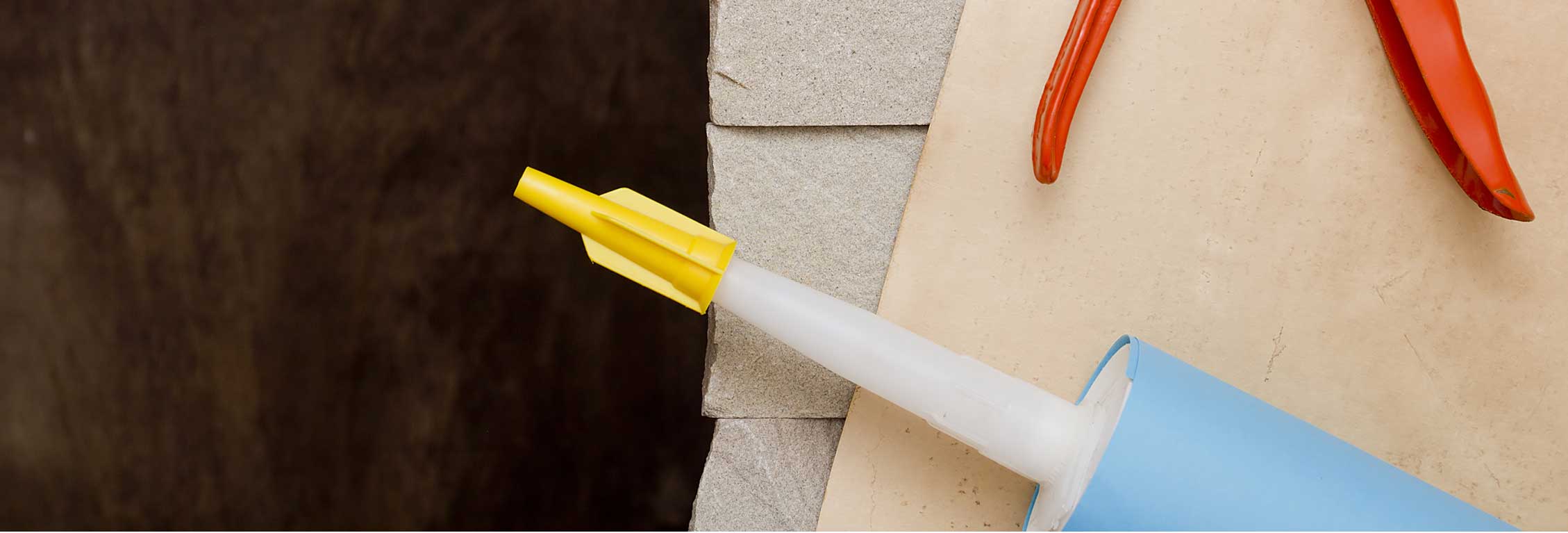 Tube of adhesive with yellow cap on tip sitting on wooden table with another tool