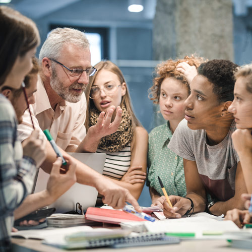 Older man talking to group of young adults with papers and notebooks on table