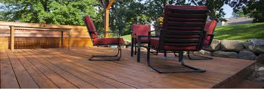 View of wooden deck with red padded metal chairs in circle with stone wall, lawn, and trees in background