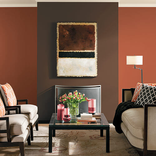 Orange and brown room with black and tan couch and chairs with glass coffee table, little decorations, and potted flowers on table