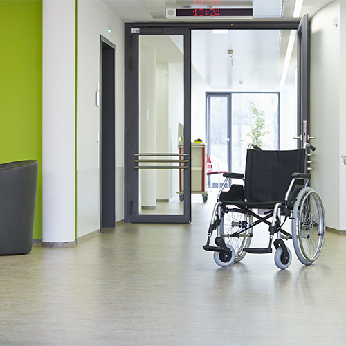 Room with white and green walls with white floor, automatic opening door, and black wheelchair