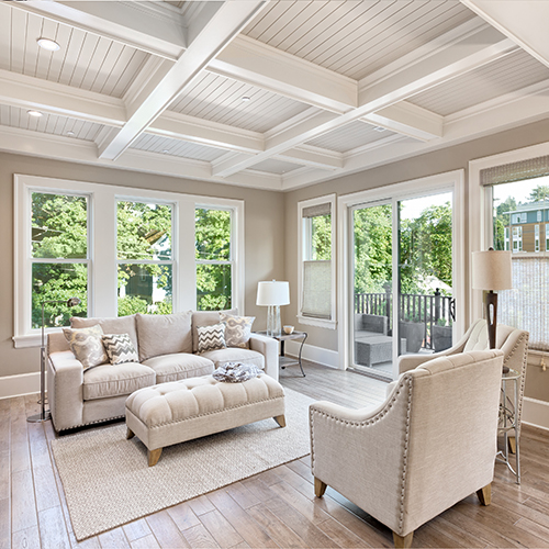 Light tan livingroom with couch, chair, and other furniture with frame designed ceiling with large windows and screen door to outside back deck 