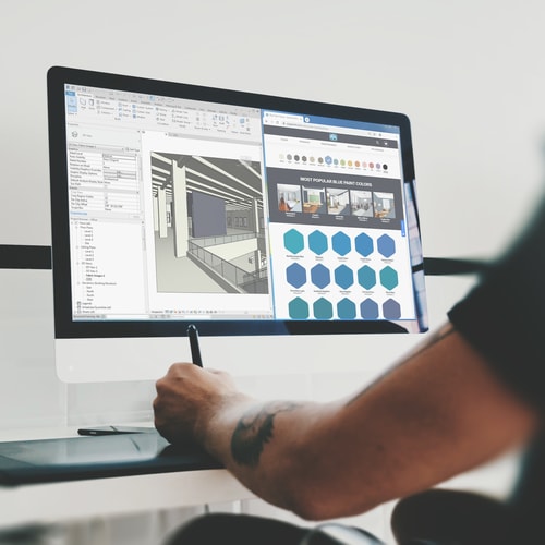 Person working on drawing tablet working on software program on large monitor in white room