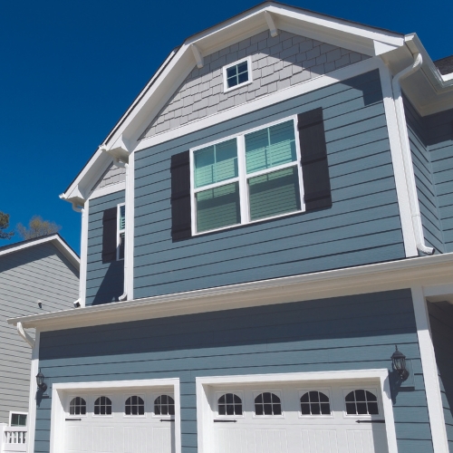 Blue paneled house with gray and white accents, windows, navy shutters, white garage, and bright blue sky