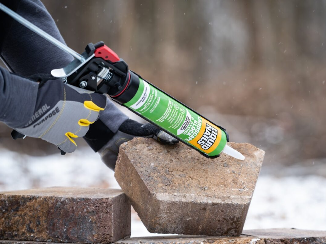 Person wearing gloves applying Liquid Nails to cut stone in a snow-covered forest