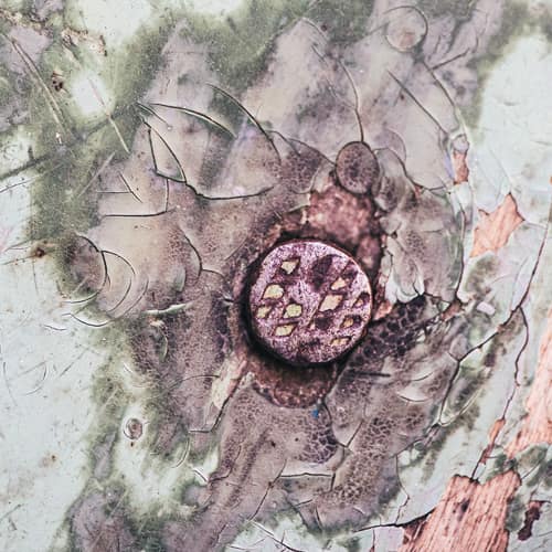 Rusted nail head with cracked and old paint around on wall