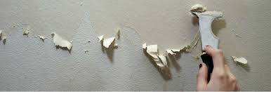 Person holding gray scrapper scraping adhesive off of white wall