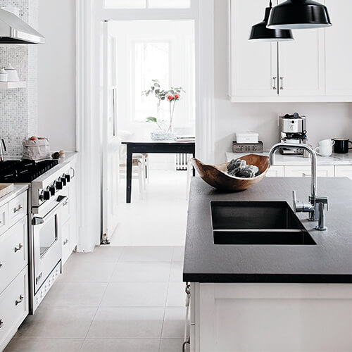 White kitchen with black counters, island top, and hanging lights with look into bright dining room