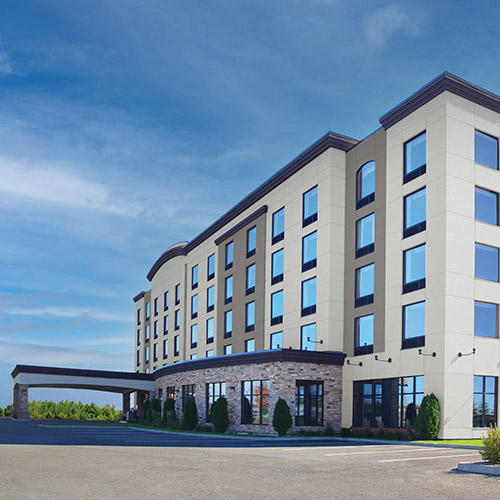 Gray and eggshell colored building with many windows, stone bottom, and parking lot on bottom