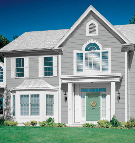 Light gray house with light gray roof with white framing around windows, light green door with lawn and small bushes