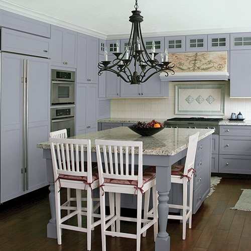 Kitchen with light gray cupboards, steel appliances, light gray and light-colored center island with white wooden chairs and dark brown flooring 