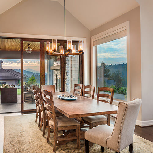 Light tan and dark brown wooden dining room with large window and screen door to outside deck, mountains, and forest in background