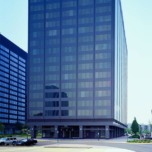 Large dark gray building with many windows with a few cars and street at bottom