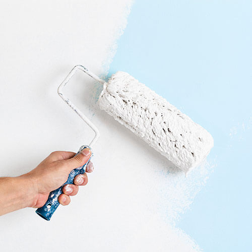 Person rolling white paint with roller on light blue wall