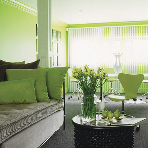 Bright green room with light gray accents with couch, black table, flowers, pears, table, chairs, and large window