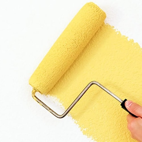 Person's hand rolling yellow paint on white surface