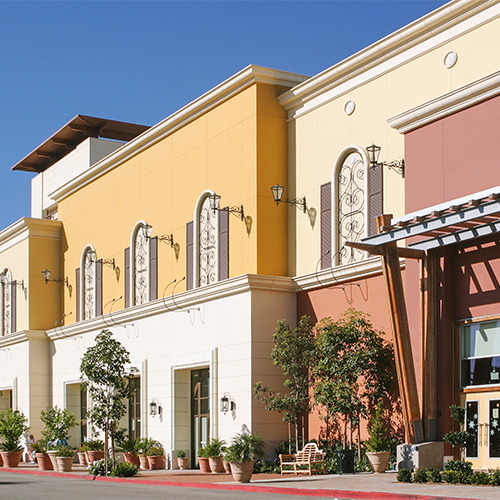 Tiered buildings painted white, yellow, pale yellow, and red with windows with potted plants on sidewalk