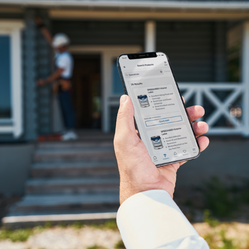Person holding phone looking at PPG paint buckets with blurred front porch and person in background