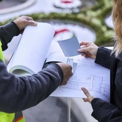View of two peoples' hands holding building plans and color samples with outside blurred background