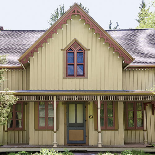 Yellow panel house with light brown roof and decorative framing with dark gray door and front porch