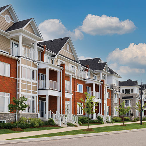 Light tan and red brick connected housing with light gray roofing and walkway with road at bottom