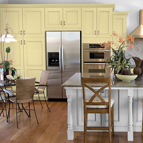 Kitchen with pale yellow cupboards, steel appliances, white and dark-colored center island with brown wooden chairs and flooring 